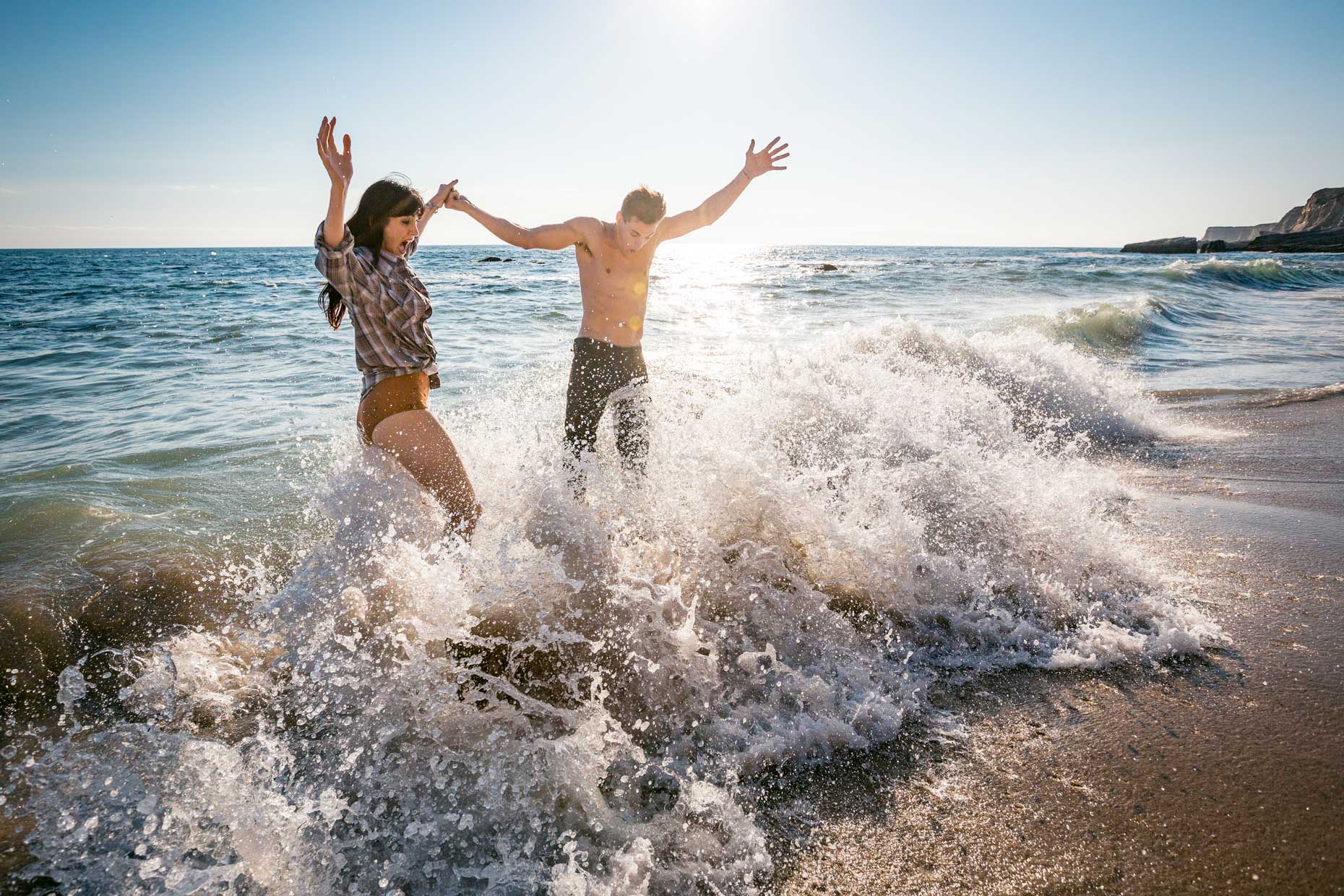 Young couple playing on the beach in the breaking waves laughing and having fun