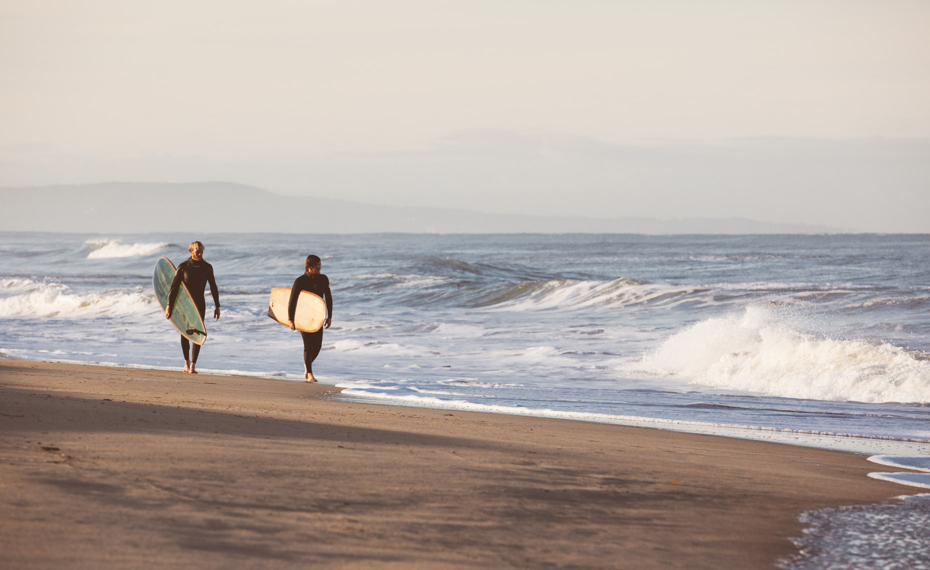 Two surfers with wooden surfboards built by Martijn Stiphout from Ventana Surfboards walking on a beach in Northern California