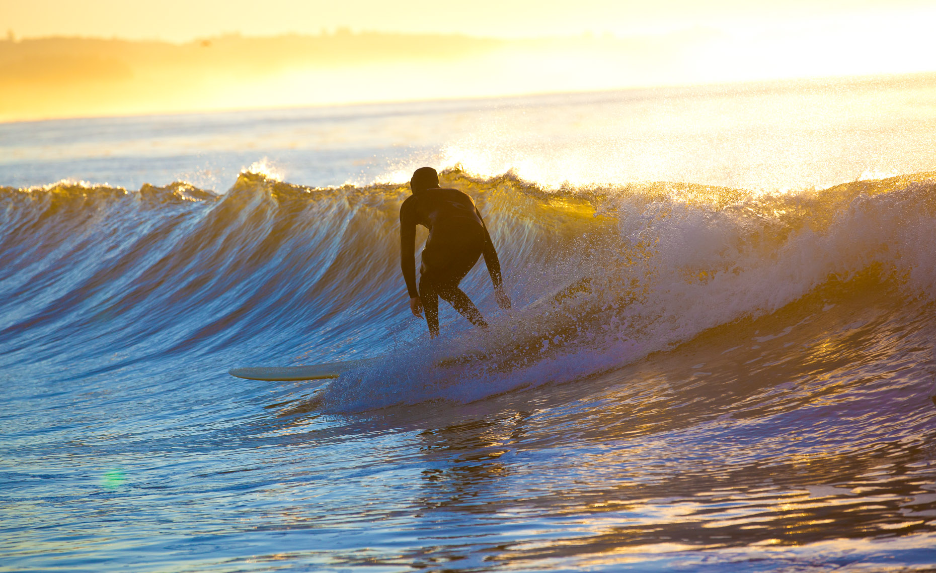 Wooden longboard surfer surfing at sunrise