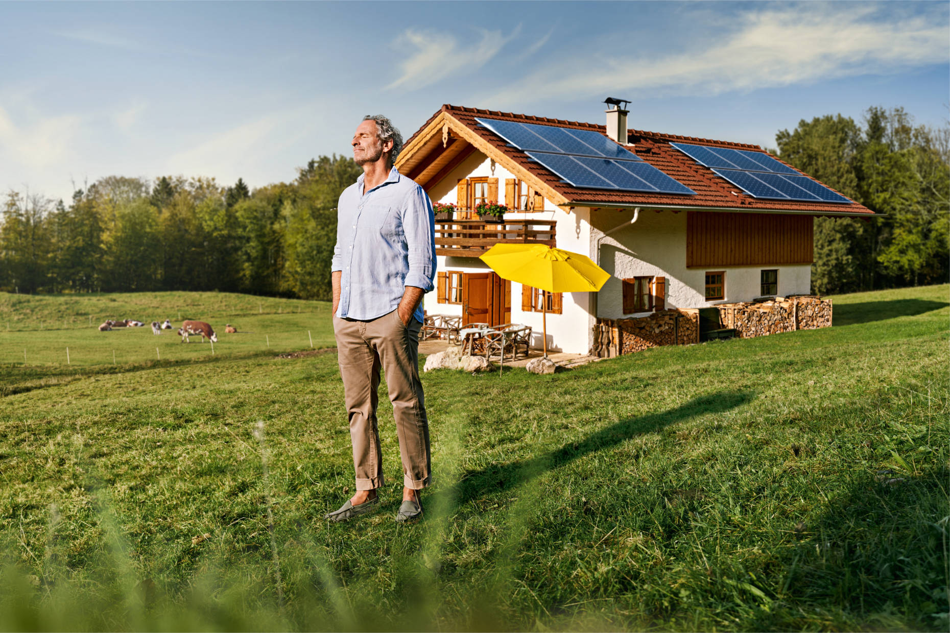 Older man standing on a field in front of his cabin with solar panels on the roof eyes closed and enjoying the sunshine