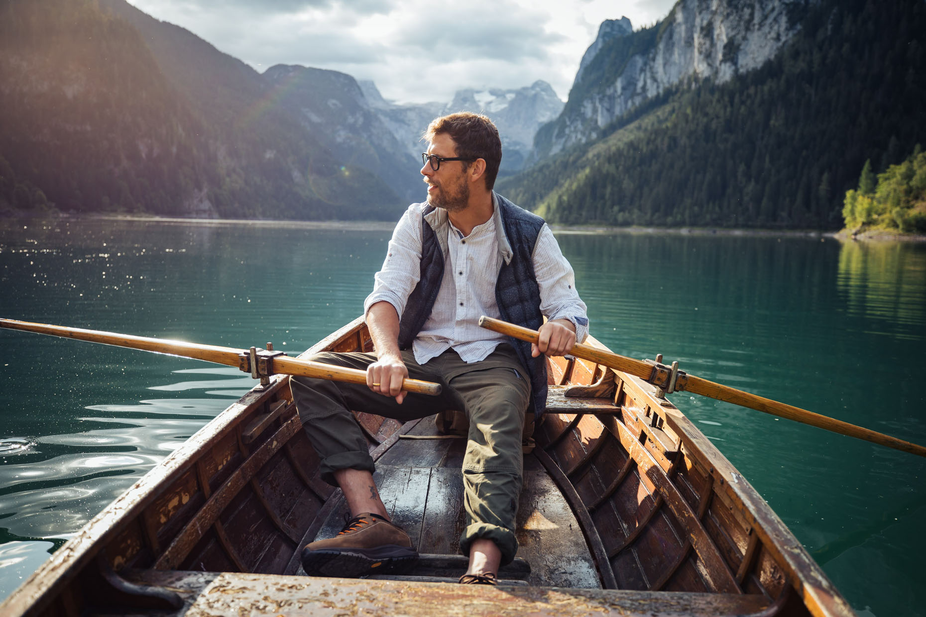 Young man with glasses rowing in a boat on a beautiful alpine lake