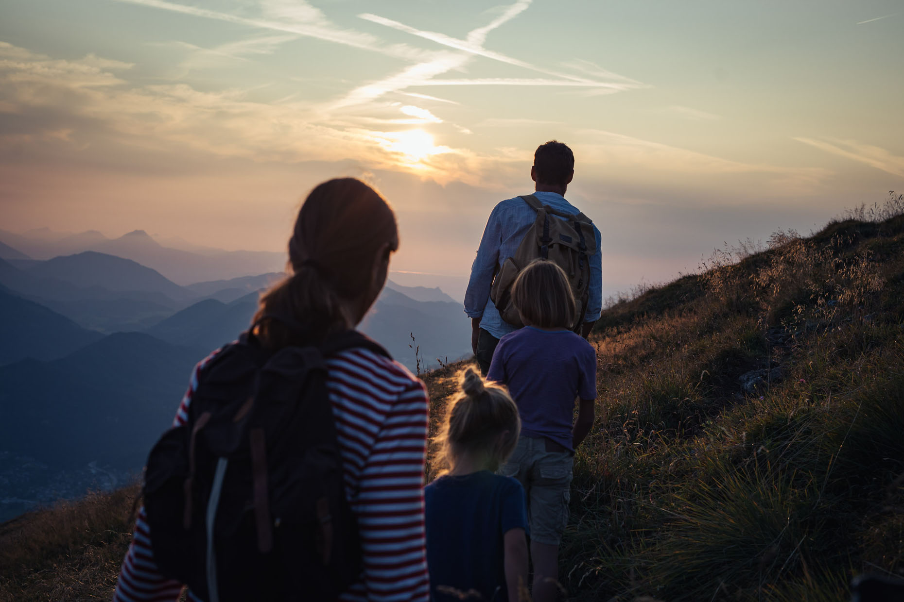 A family with two small boys hiking on a grassy mountain ridge in the beautiful golden light just before sunset
