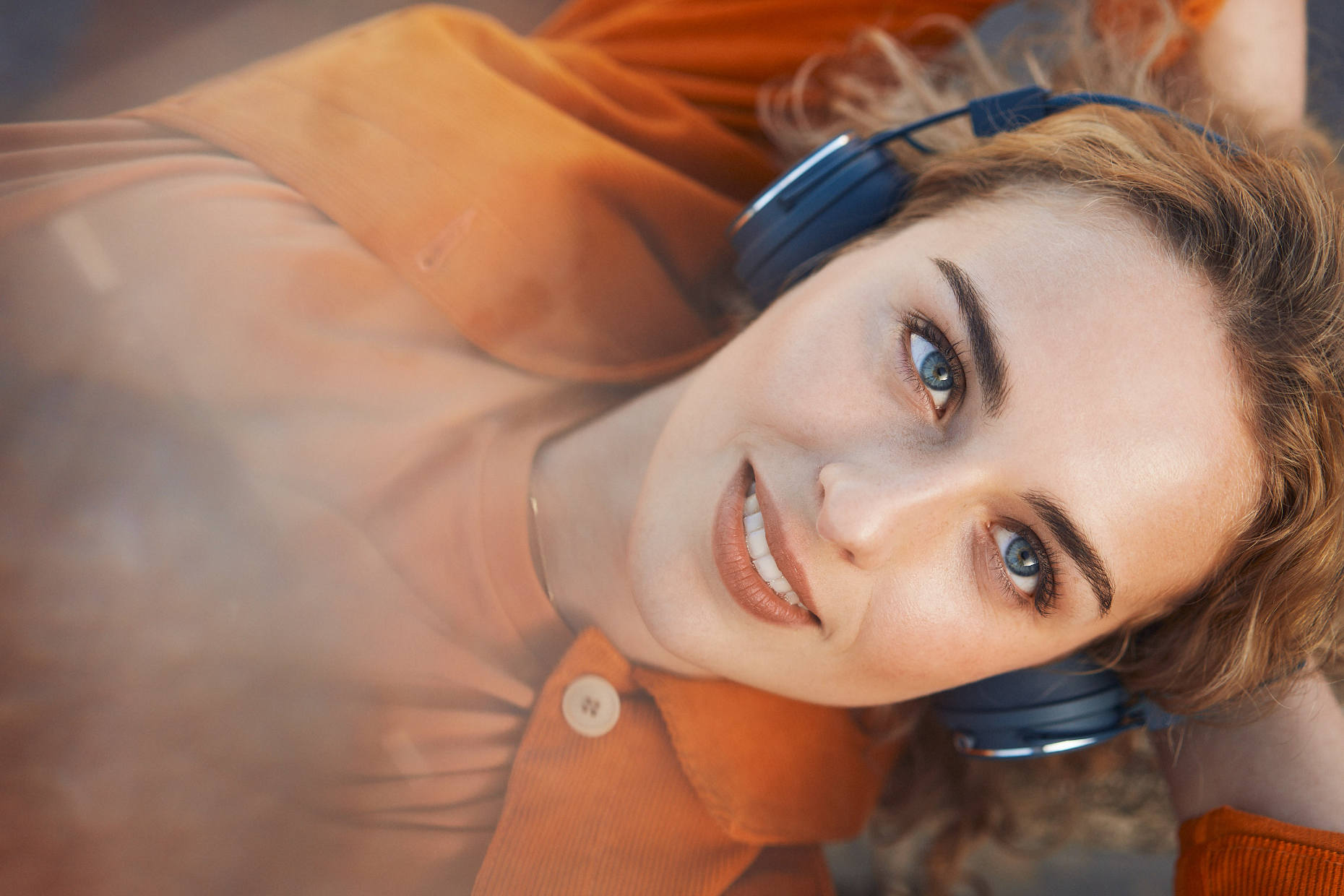 Smiling blonde woman with blue eyes wearing headphones with a visionary facial expression