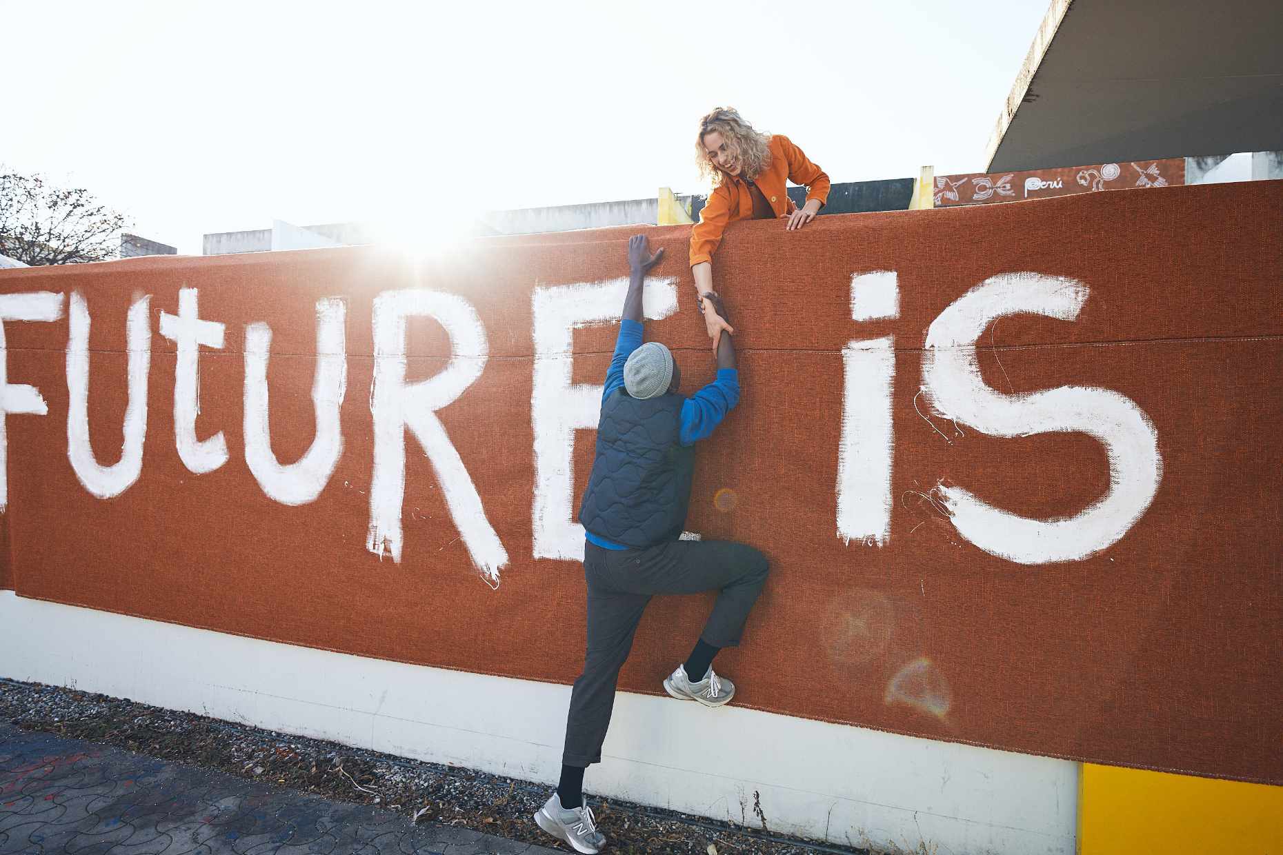 A young woman and a young man climbing a wall with a protest banner showing the word future 