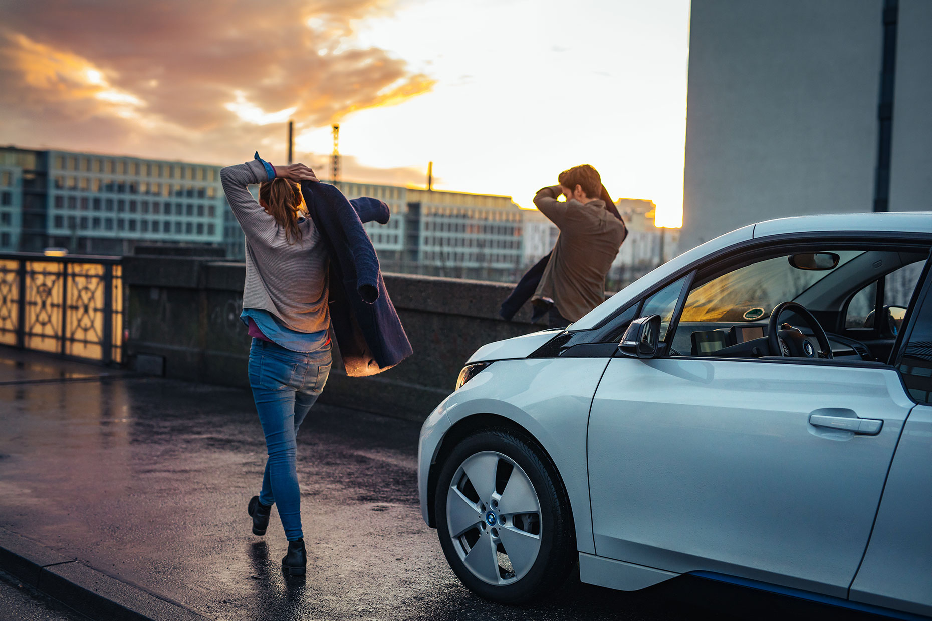 Young couple on a bridge at sunset walking away from a BMW i3 electric car